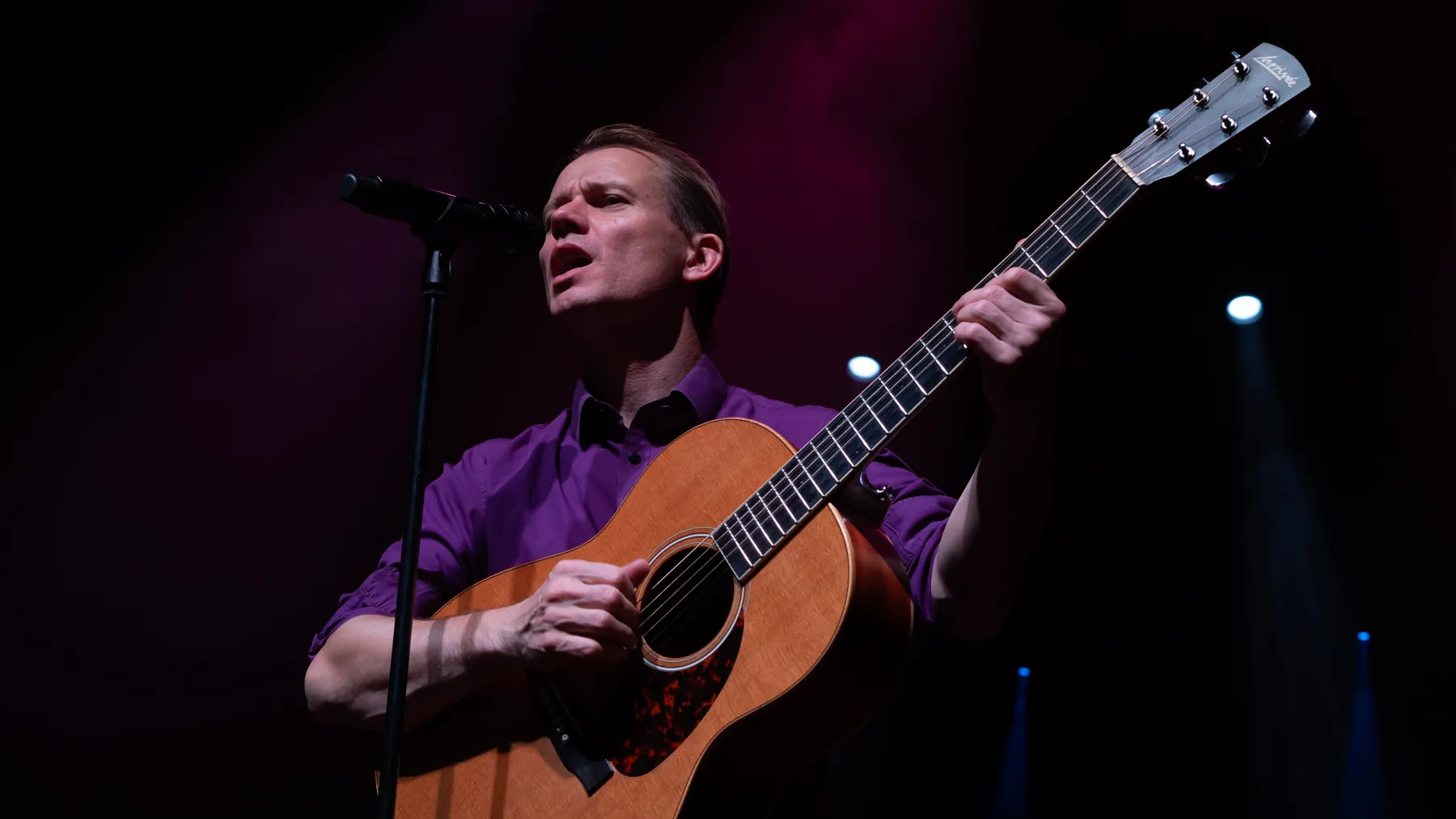 Mads med guitar i lilla skjorte under magenta projektører
